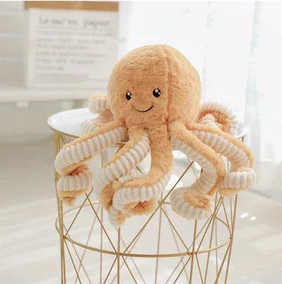 Peluches pieuvre orange avec tentacules bouclés blanches posée sur une table métallique dorée