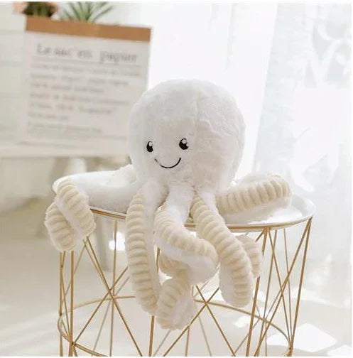 Peluche pieuvre blanche souriante aux tentacules torsadés posée sur une table en métal doré