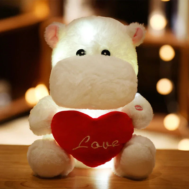 Peluche hippopotame blanc lumineux tenant un cœur rouge avec le mot Love en intérieur chaleureux